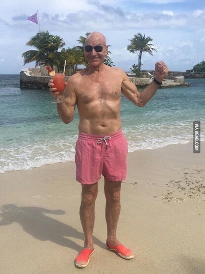Sir Patrick Stewart, wearing only pink swimming trunks, on a tropical beach, smiling while doing a big arms pose and holding a fancy drink.