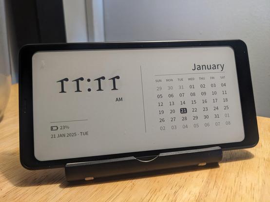 Photo of my Boox Palma e-ink Android device on screensaver mode, which displays the time, the calendar, and the battery level. Unfortunately, the font they're using for the numbers is so unusually stylized, the current time (11:11) instead looks like "rr:rr."